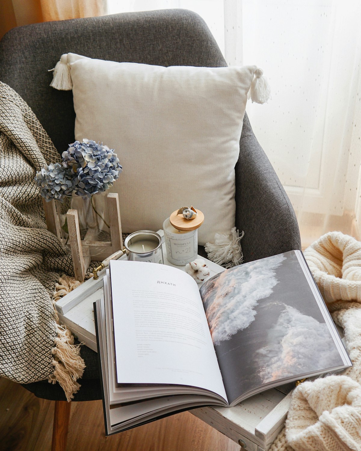 A reading chair with a cushion, a blanket and an open book
