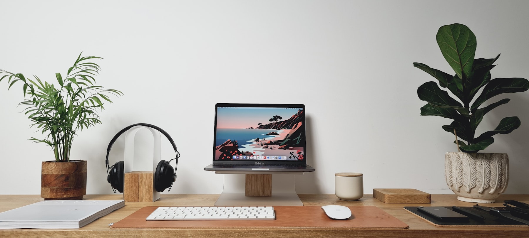A bright desk with green plants on both sides of a laptop
