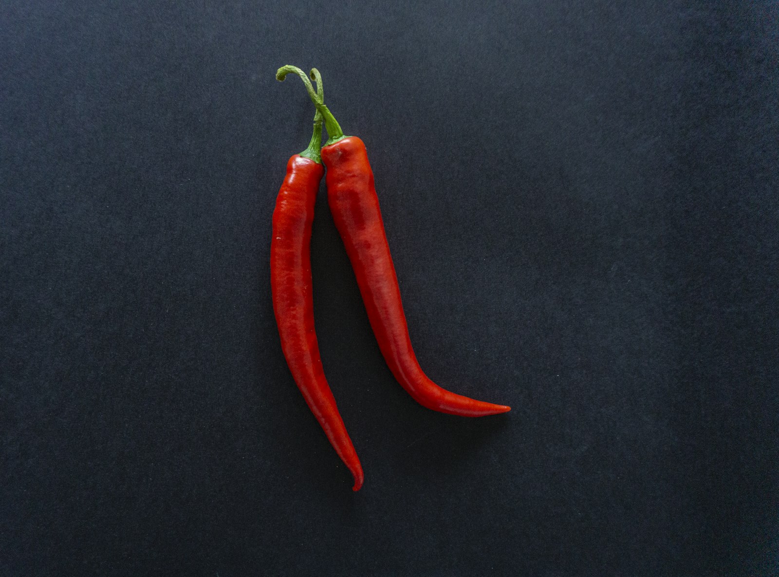 Two red chili peppers on a black background
