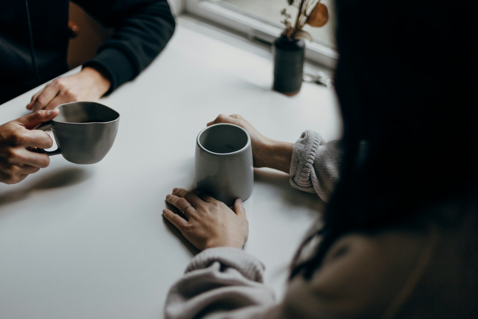 Two people talking over mugs at a cafe table