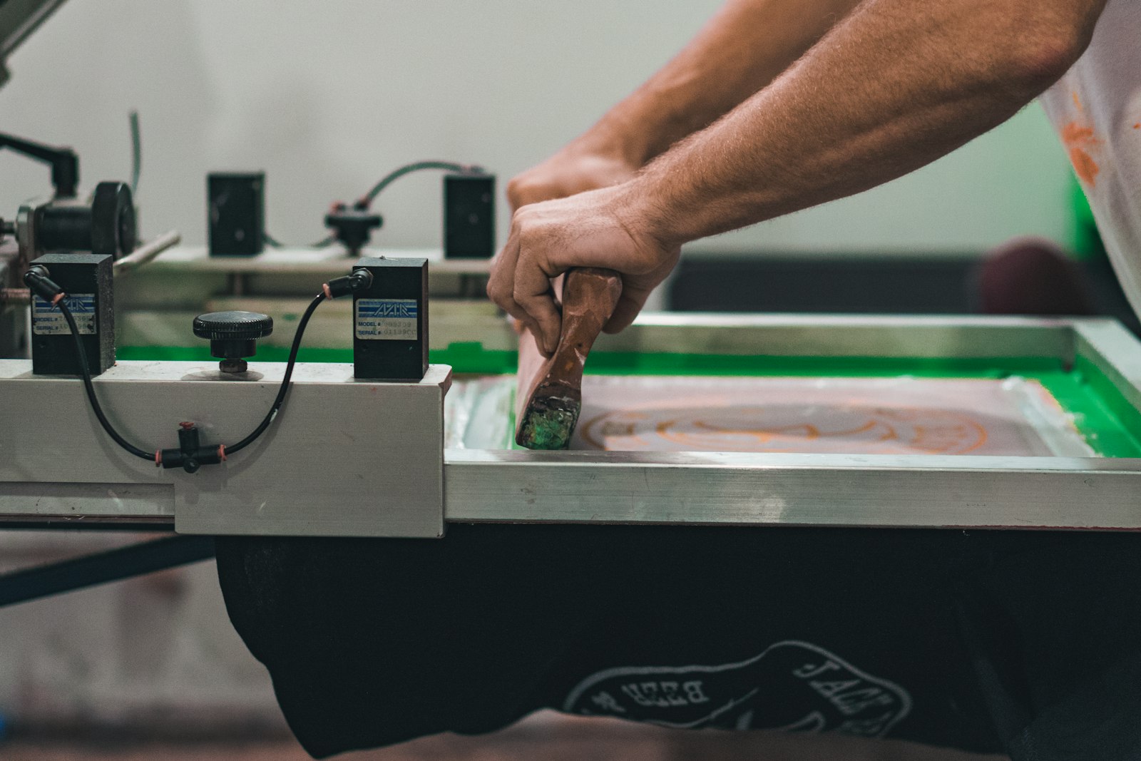 A squeegee pulling ink across a screen printing frame