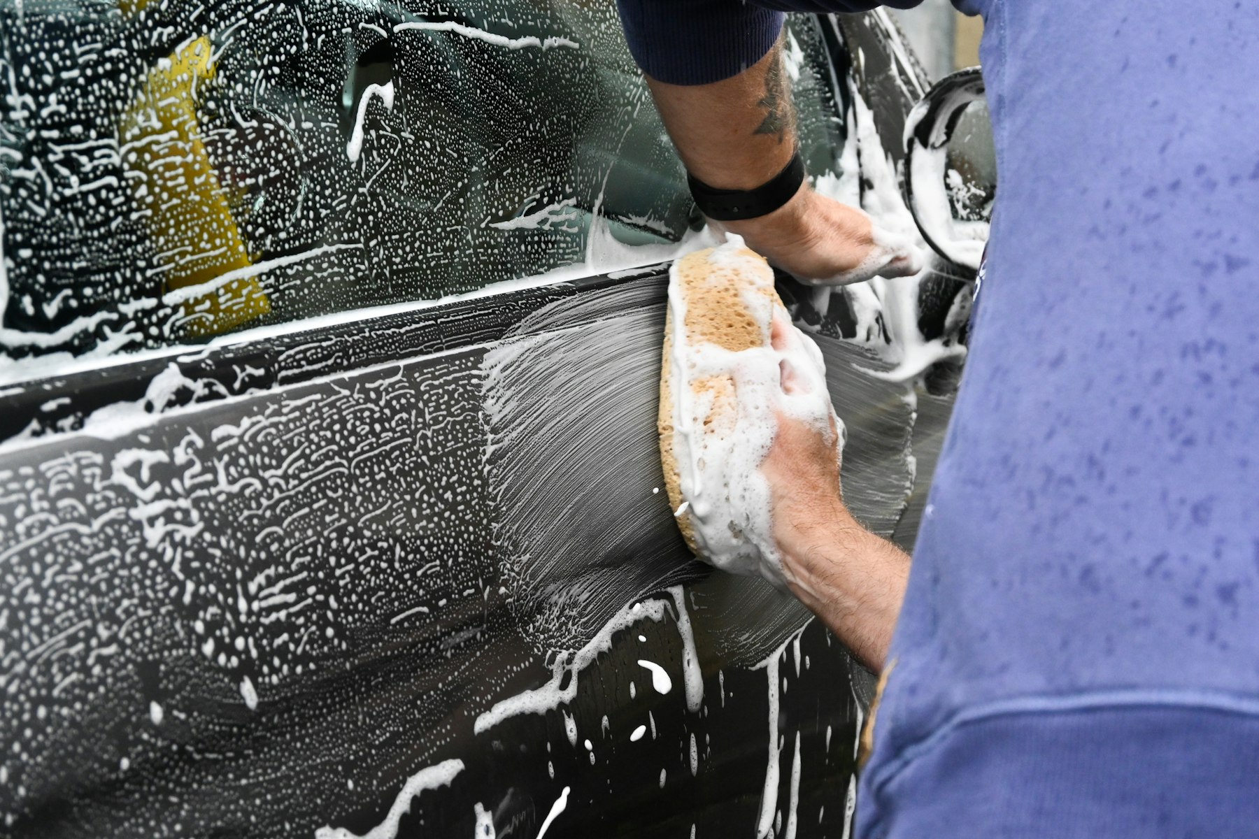Hand washing a car door with a foam sponge